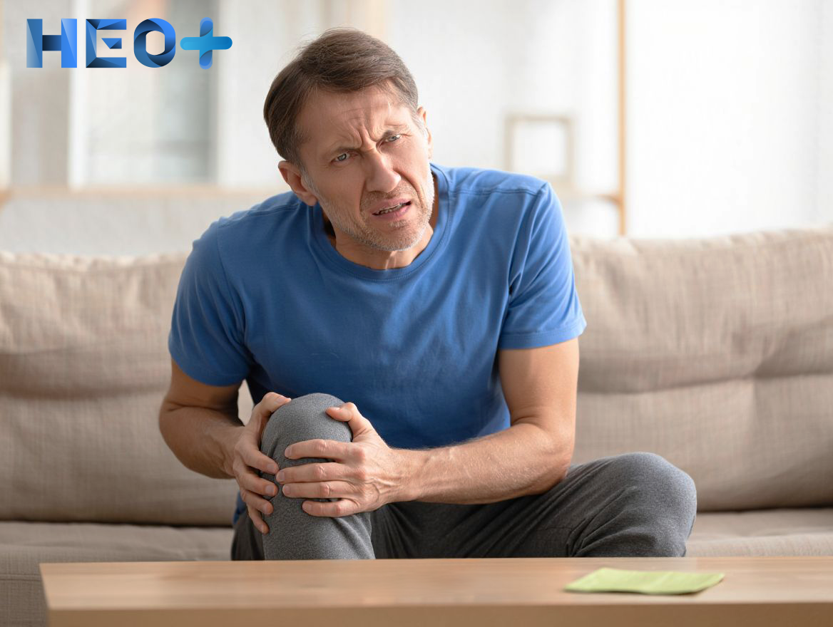 мужчина с болью в ноге сидит на диване и держится за свою ногу